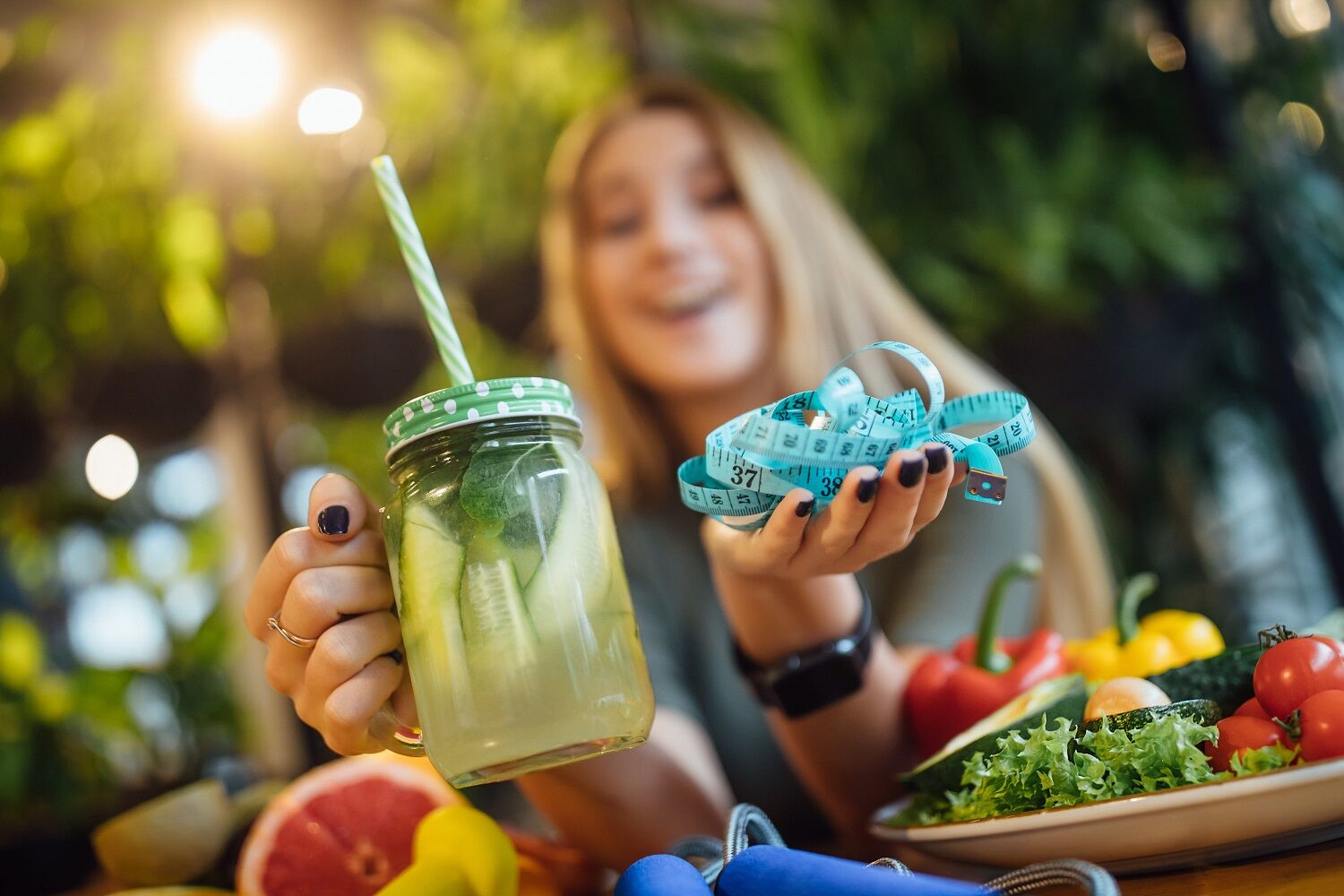 1784180459 Blonde Fithess Girl Sit Table Holding Fresh Smoothie Measure Diet Time Concept (1)